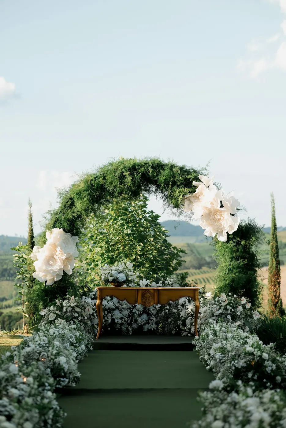 Arche de feuillage et de grandes fleurs blanches au bout d’une allée bordée de fleurs blanches, en plein air