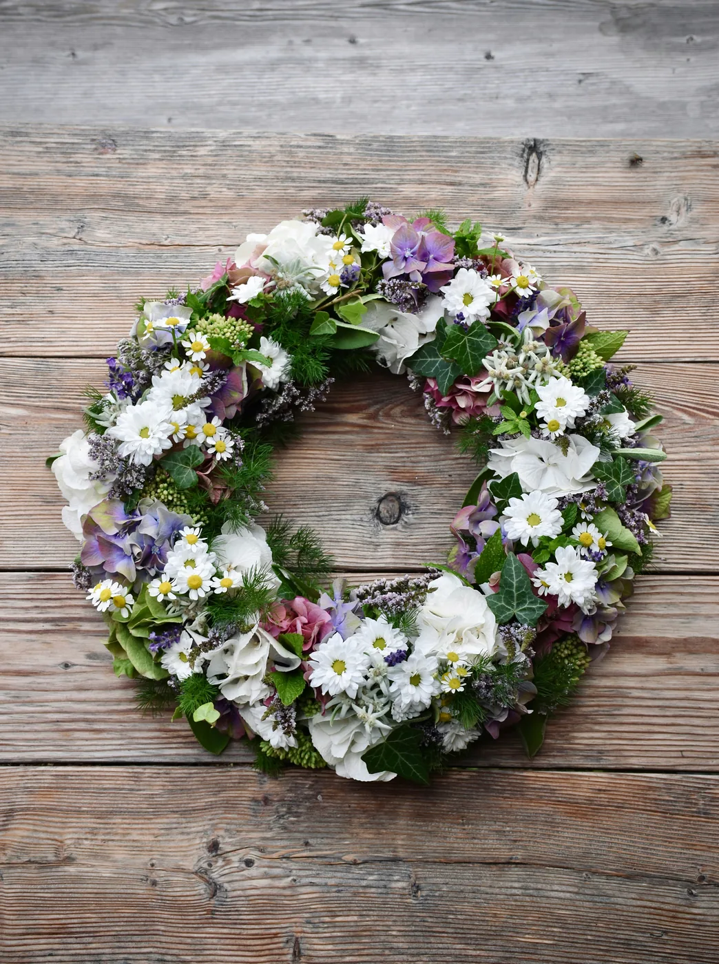 Couronne de fleurs blanches et violettes et de feuillage vert, posée sur du bois